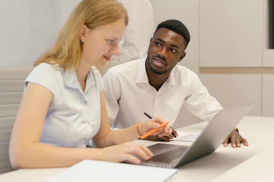 African American man and Caucasian woman collaborating at a laptop in an office environment.