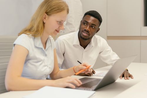 Free African American man and Caucasian woman collaborating at a laptop in an office environment. Stock Photo