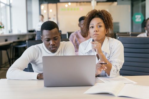Free Two young professionals focused on a laptop in a modern office setting, collaborating on a project. Stock Photo