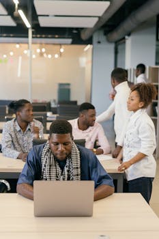 Group of professionals working together in an open-plan office space, focusing on technology and teamwork.