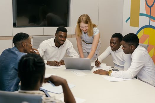 Multicultural group engaging in teamwork around a laptop in a conference room.