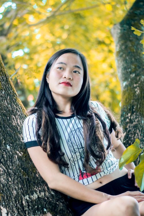 Free A young woman outdoors leaning against a tree, enjoying a peaceful moment. Stock Photo