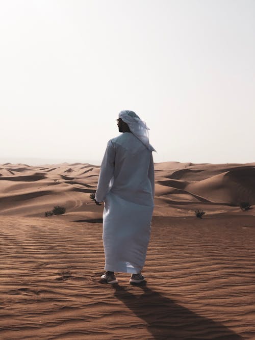 Man in White Thobe Walking on Desert Sand