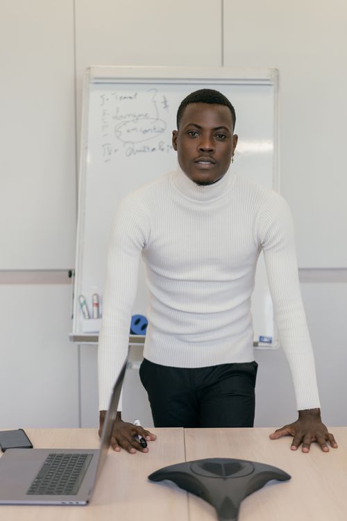 Free A confident businessman in a white turtleneck presenting in a modern office setting. Stock Photo