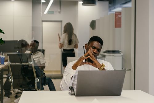Free African American man concentrating at his laptop in a contemporary office environment with coworkers. Stock Photo