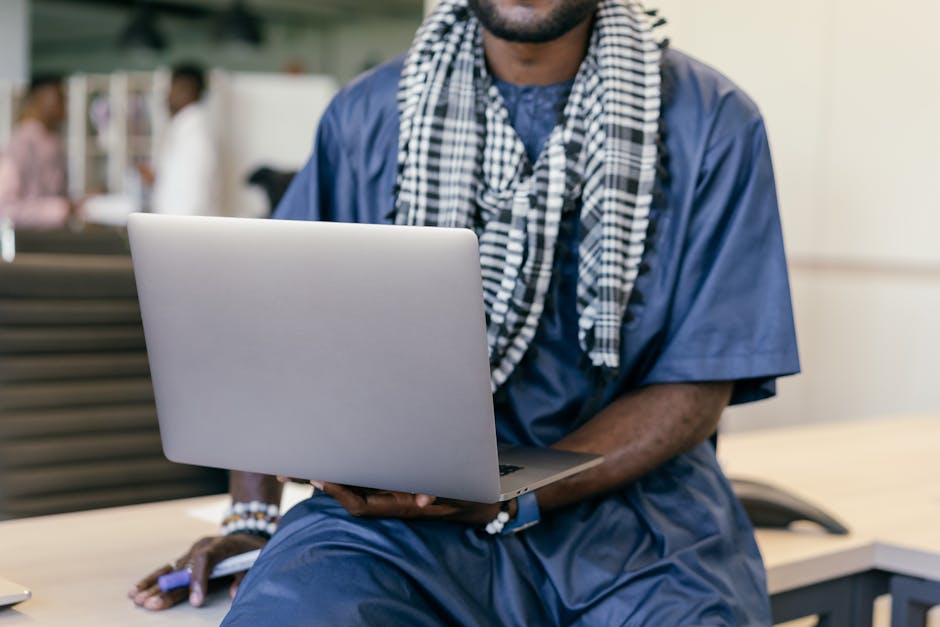 African man in traditional clothing using a laptop in an office setting, merging culture and technology.