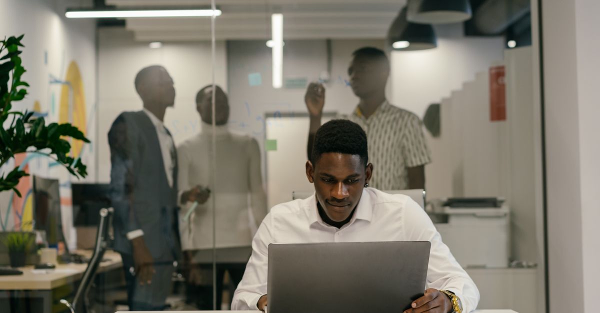 Um homem de camisa branca trabalha intensamente em um laptop em uma mesa de escritório moderna.