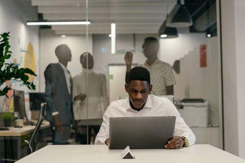 Free A man in a white shirt works intently on a laptop at a modern office desk. Stock Photo