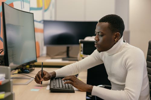 Man in White Sweater Using a Computer at Work
