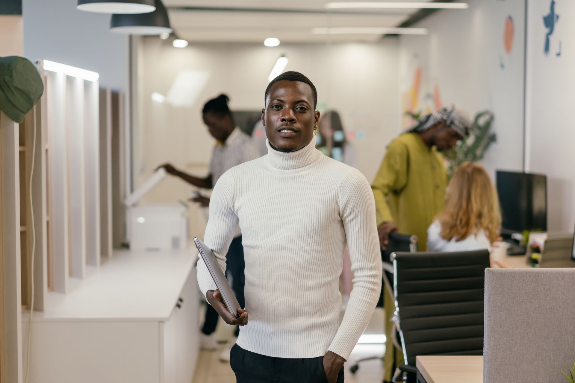 Young professional man in white turtleneck standing confidently in a modern office environment.