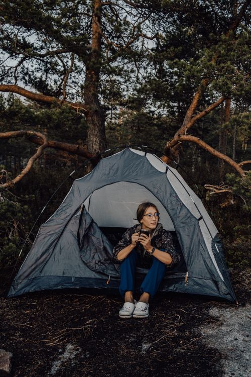 Free A young woman relaxes with a hot drink by her tent in the serene Ruskeala forest. Stock Photo