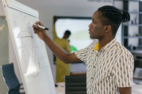 Free Young professional presenting a business strategy on a whiteboard in a modern office setting. Stock Photo