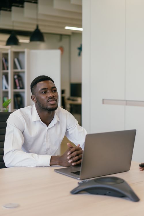 Free Young man in formal attire working at a laptop in a modern office space. Stock Photo