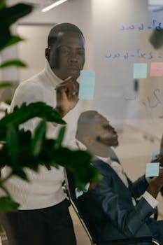 Two men collaborating in an office using sticky notes and a glass board.