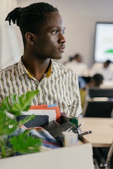 Focused man in a modern office setting holding personal items, deep in thought.