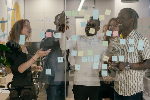 A diverse group of colleagues collaborates using sticky notes on a glass wall in an office.