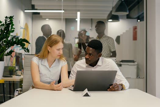 Colleagues collaborating in a modern office setting, discussing ideas at a laptop.