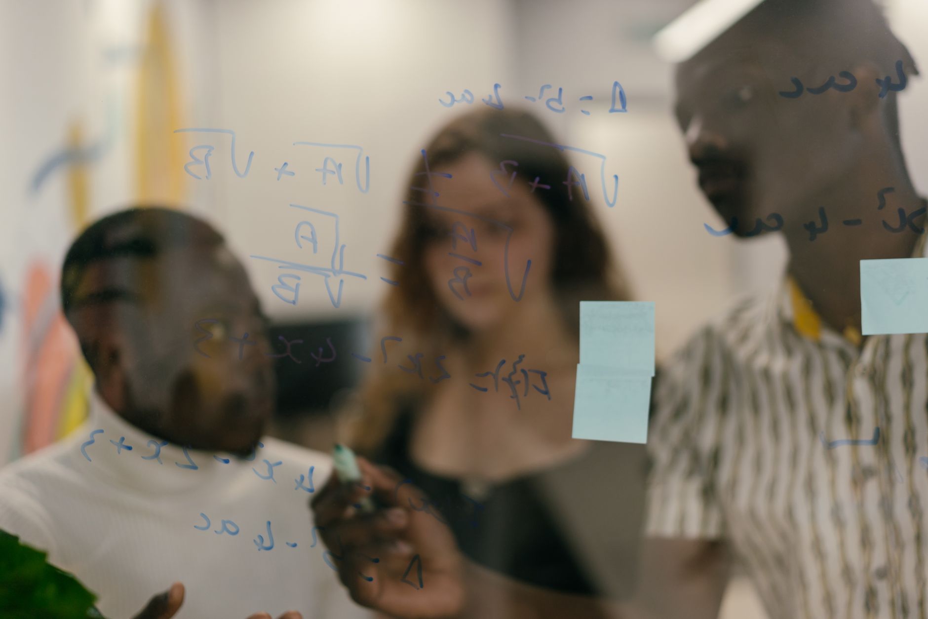 Diverse group of people solving math equations on a glass panel indoors.