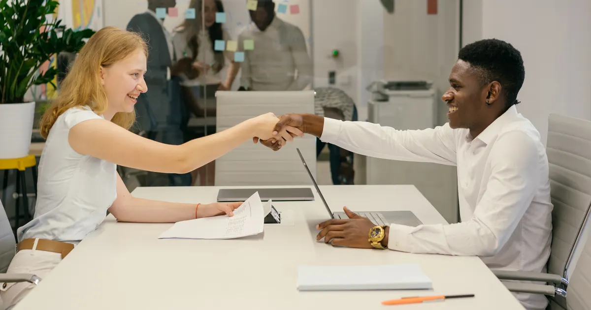 A man and a woman shaking hands across a table with a document on it, representing third-party AI tool risk assessment template 2026