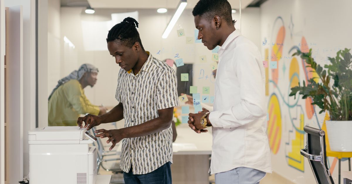Two colleagues using a printer in a modern office, showcasing teamwork and collaboration.