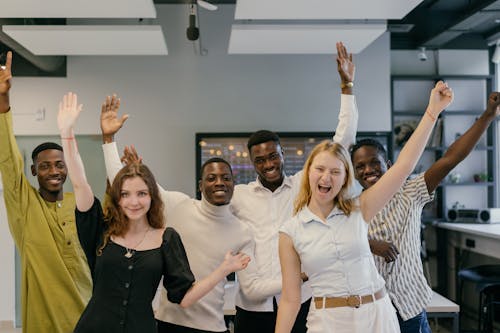 Free Employees Raising their Hands while Smiling at the Camera Stock Photo
