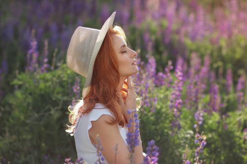 Free Woman in a sun hat smiles with eyes closed, surrounded by a vibrant lavender field, during a summer's day. Stock Photo