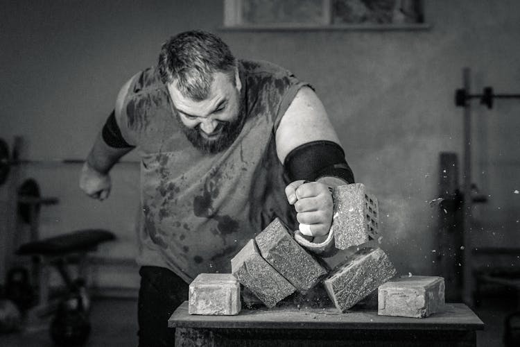 Grayscale Photography Of A Man Hitting The Blocks Of Cement On The Table