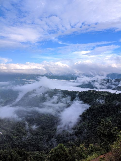 Free Stunning high-altitude view of mountainous terrain covered in mist and clouds under a blue sky. Stock Photo