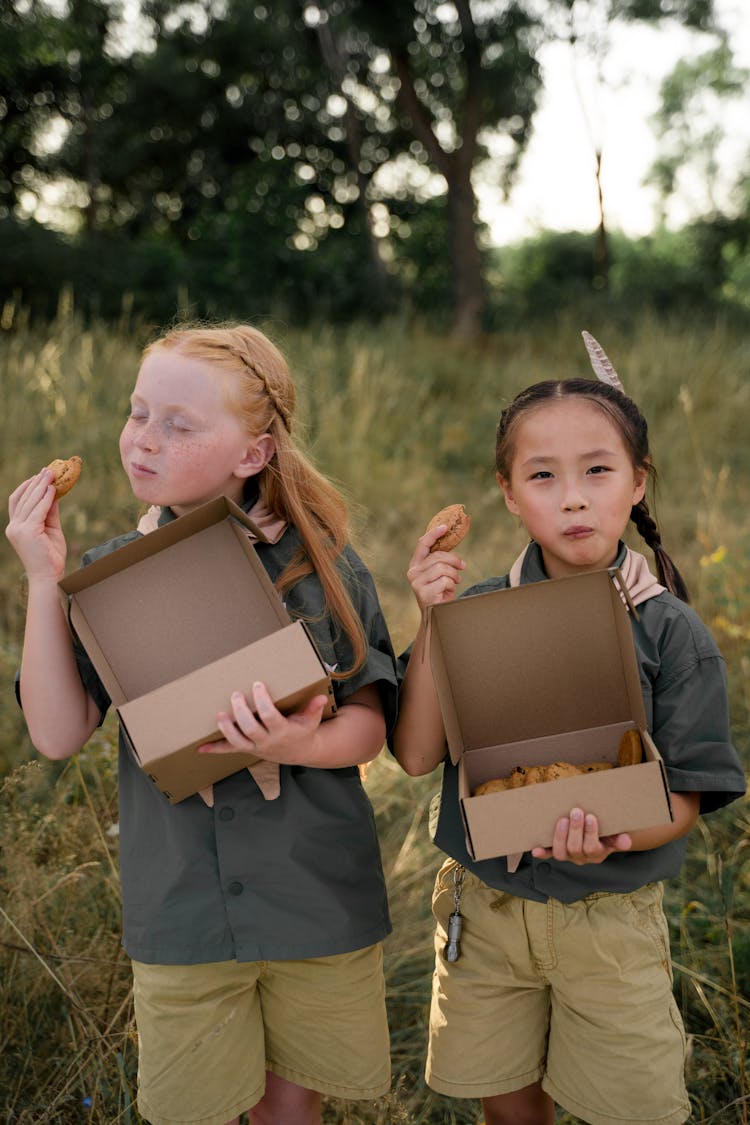 Adorable Girls Eating Cookies With Standing On Green Grass 