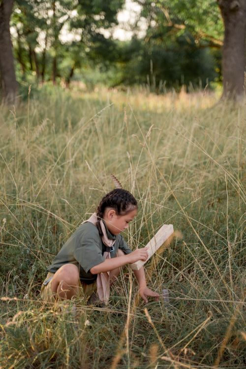 Free Asian child hammering a wooden stake at summer camp in a grassy outdoor setting. Stock Photo