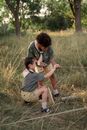 Man in Black T-shirt and Brown Shorts Holding Girl in Brown Dress on Green Grass