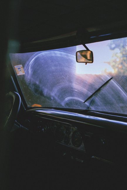 Moody interior view of a vintage car through a foggy windshield, highlighting steering wheel and rear view mirror.