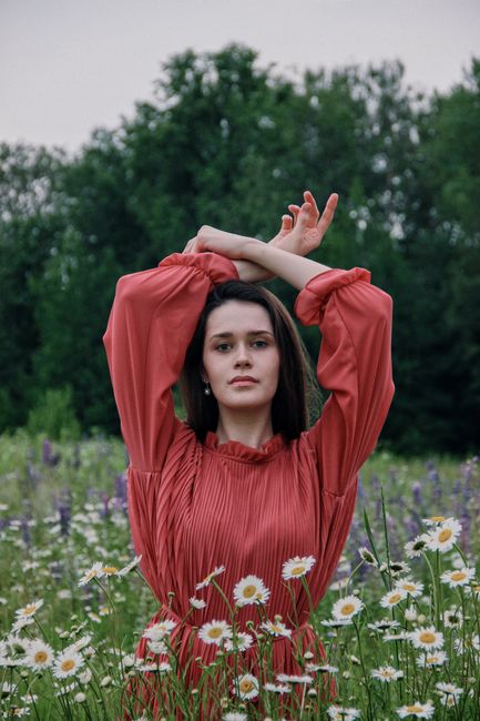 Woman in red dress stands elegantly among daisies in a lush field, evoking serenity.