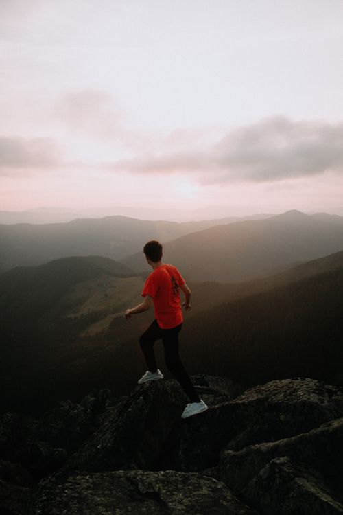 Free A solitary hiker in a red t-shirt surveys a mountainous landscape at sunset. Stock Photo