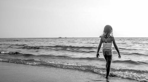 Free Grayscale Photo of Girl Walking on Seashore With White Spaghetti Strap Top Stock Photo