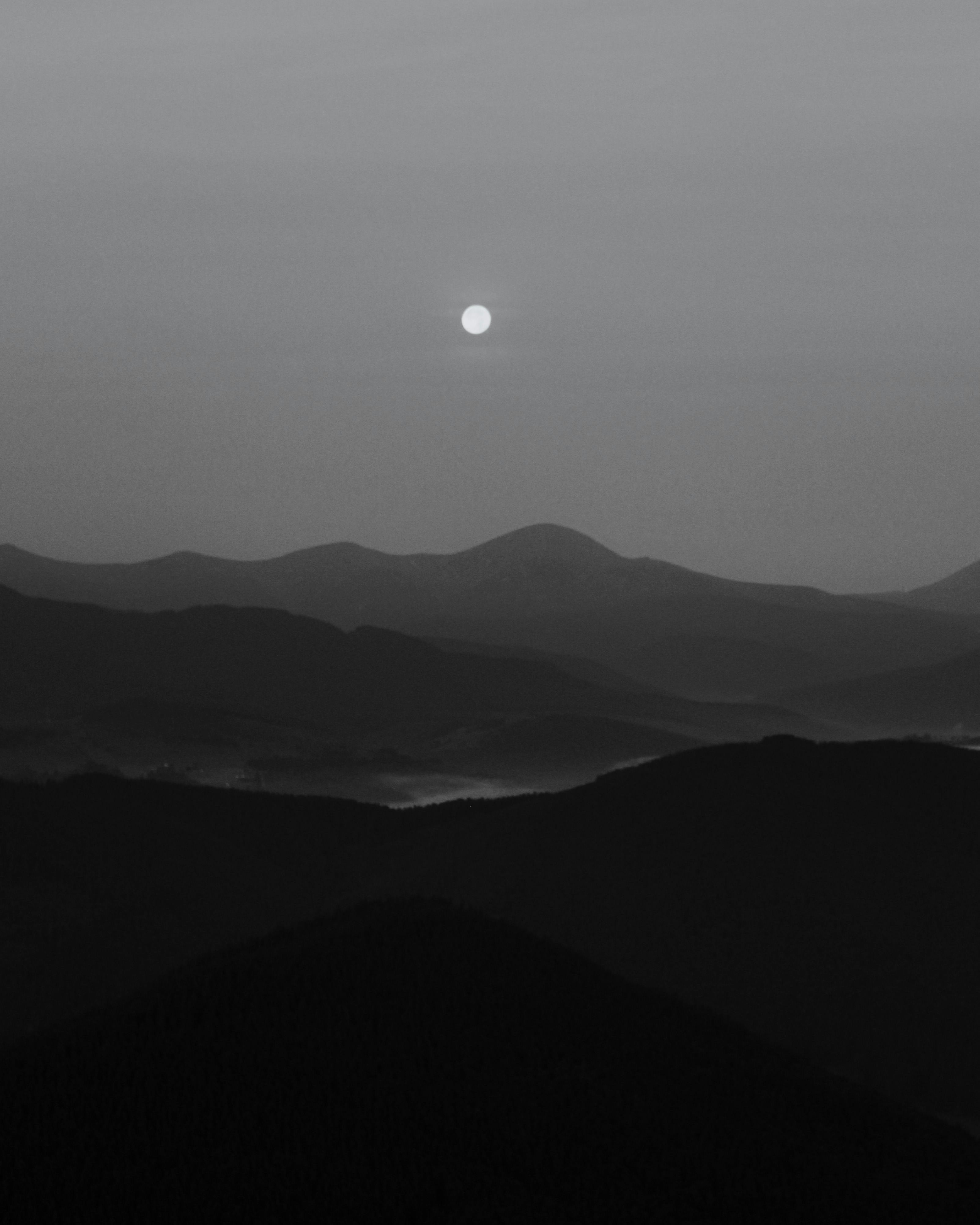 A serene black and white landscape of mountains under the moonlight, capturing fog and tranquility.