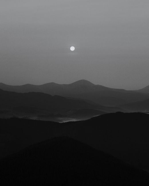 A serene black and white landscape of mountains under the moonlight, capturing fog and tranquility.
