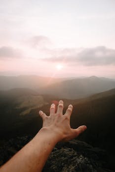 A hand reaching out towards a distant mountain sunrise, capturing a sense of adventure.
