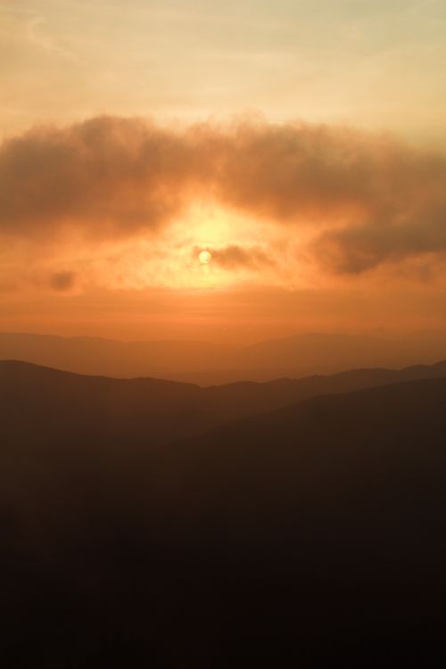 Free A stunning sunset casting a warm glow over a silhouette of mountains and clouds. Stock Photo