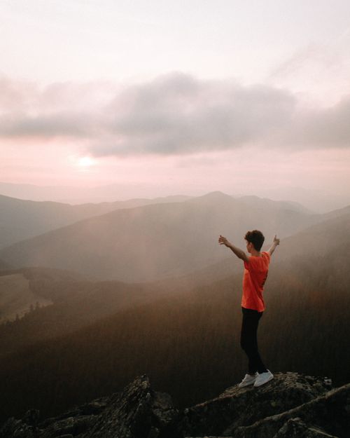 Free A hiker stands triumphantly on a mountain peak at sunset, enveloped in mist and nature. Stock Photo