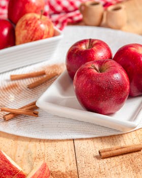 Red apples with cinnamon sticks on a wooden table, perfect for a fresh and delicious snack idea.