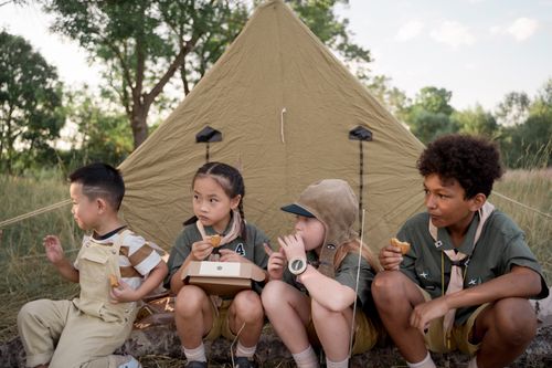 Free Group of children sitting by a tent enjoying a camping meal together in nature. Stock Photo