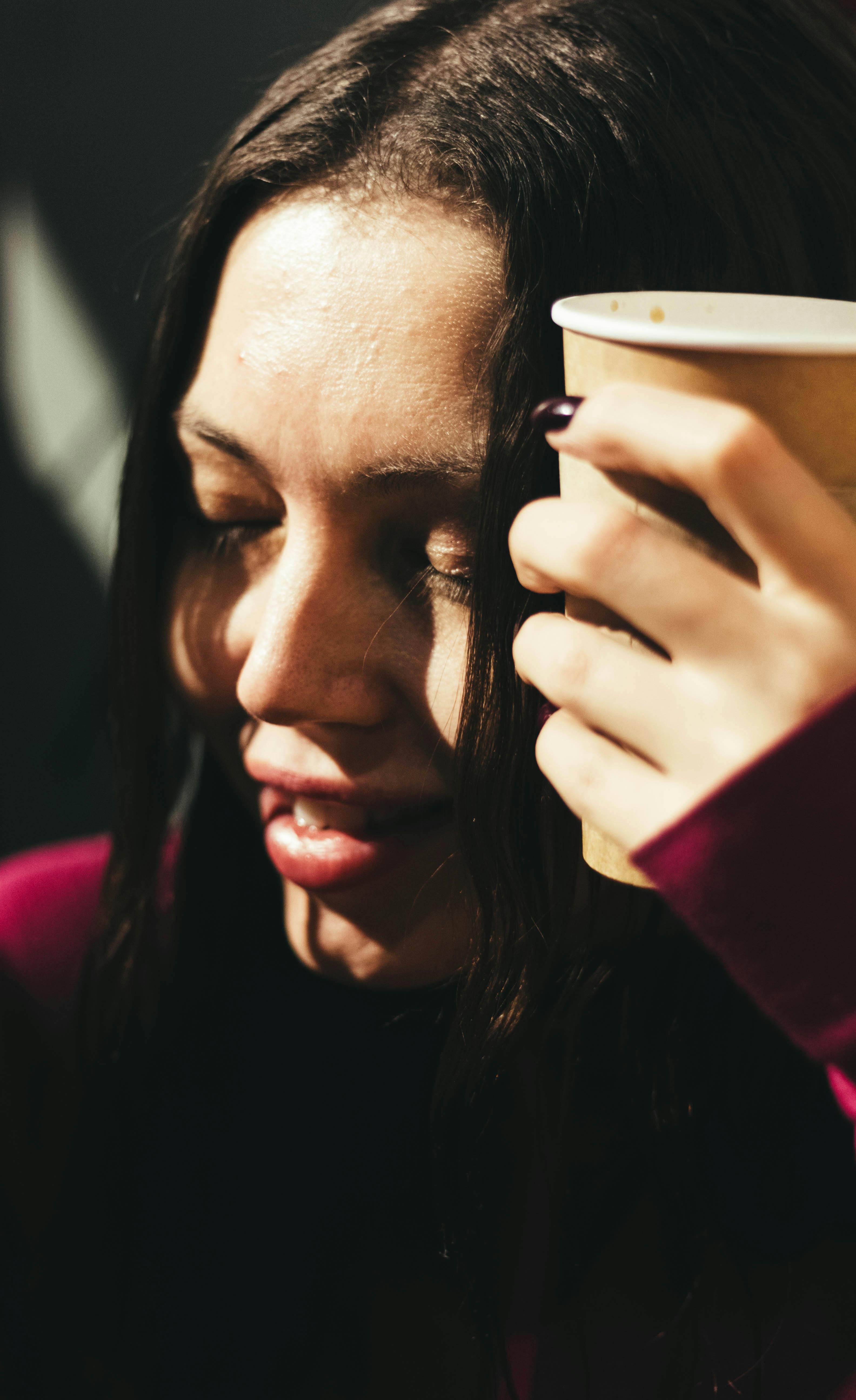 Captured moment of a young woman savoring a warm drink, showcasing relaxed expression.