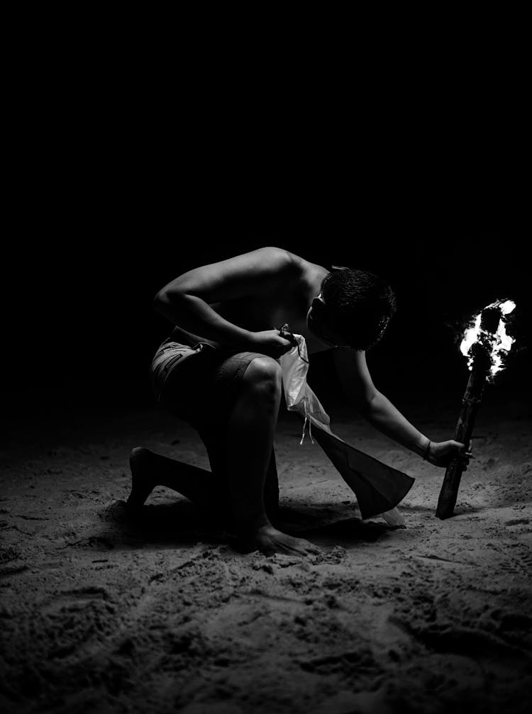 Black Photograph Of A Man With Burning Torch Kneeling On The Ground