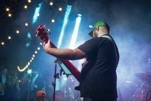 Back view of a musician playing guitar on stage during a vibrant concert night under string lights.