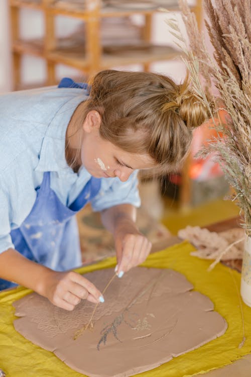 Artist in Blue Shirt and Apron Working on an Art Piece