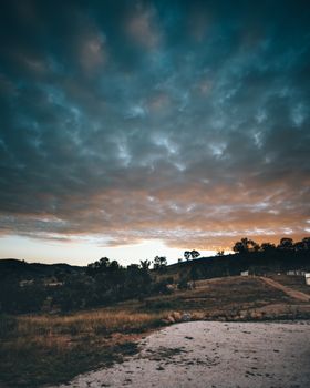 A scenic view of a rural landscape with rolling hills and clouds during sunset.