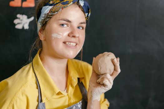 Smiling young woman holding clay in art studio, showcasing artistic expression and craftsmanship.