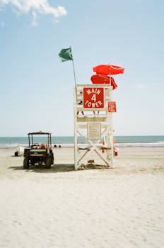 Lifeguard tower with red umbrellas and beach buggy on a sunny Rhode Island beach.
