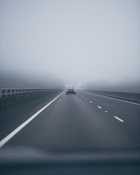 A solitary car drives along a foggy highway, highlighting calm travel.